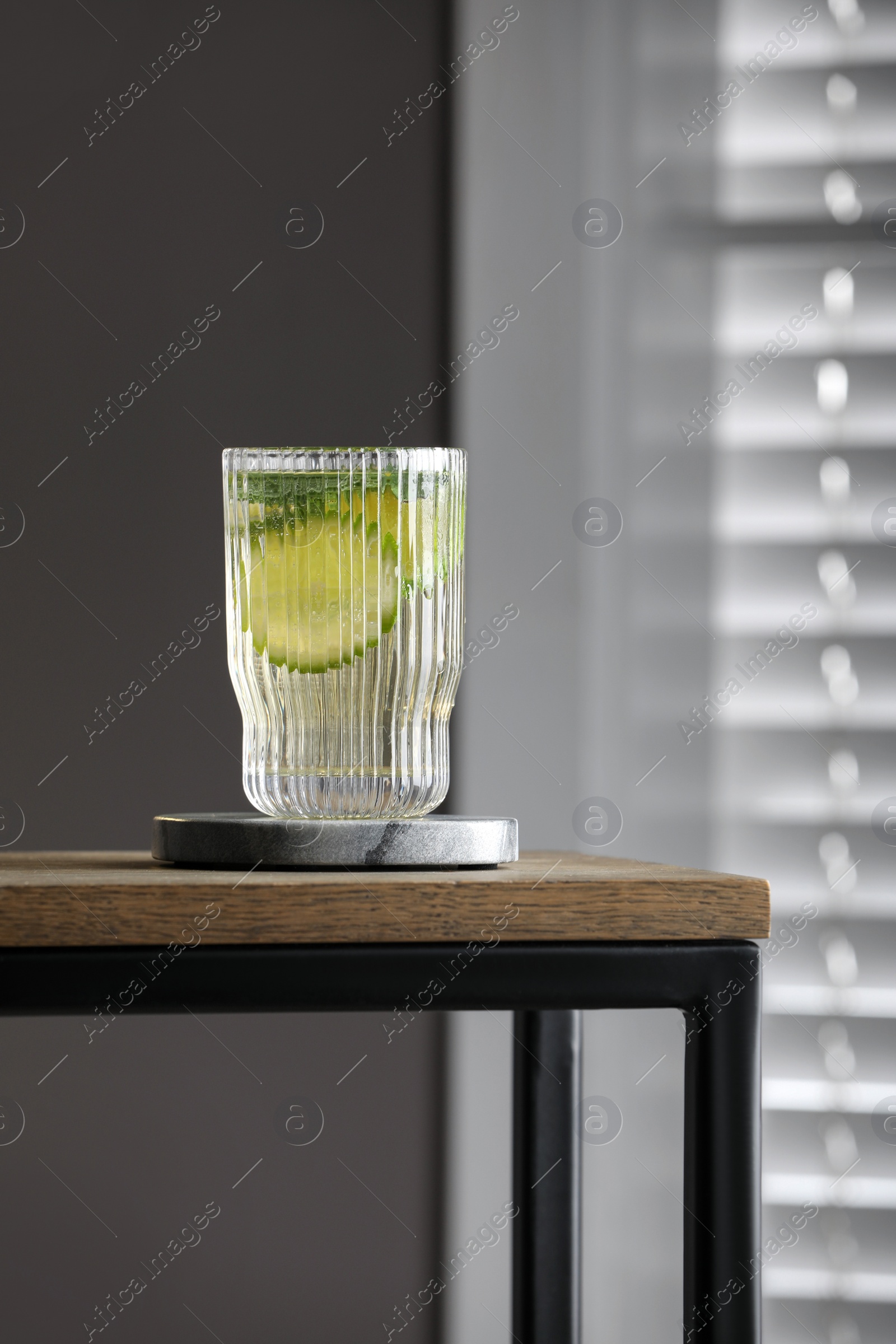 Photo of Glass of lemonade and stylish cup coaster on wooden table in room