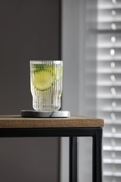 Glass of lemonade and stylish cup coaster on wooden table in room