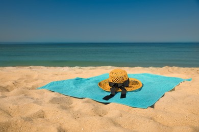 Turquoise beach towel with hat on sand near sea
