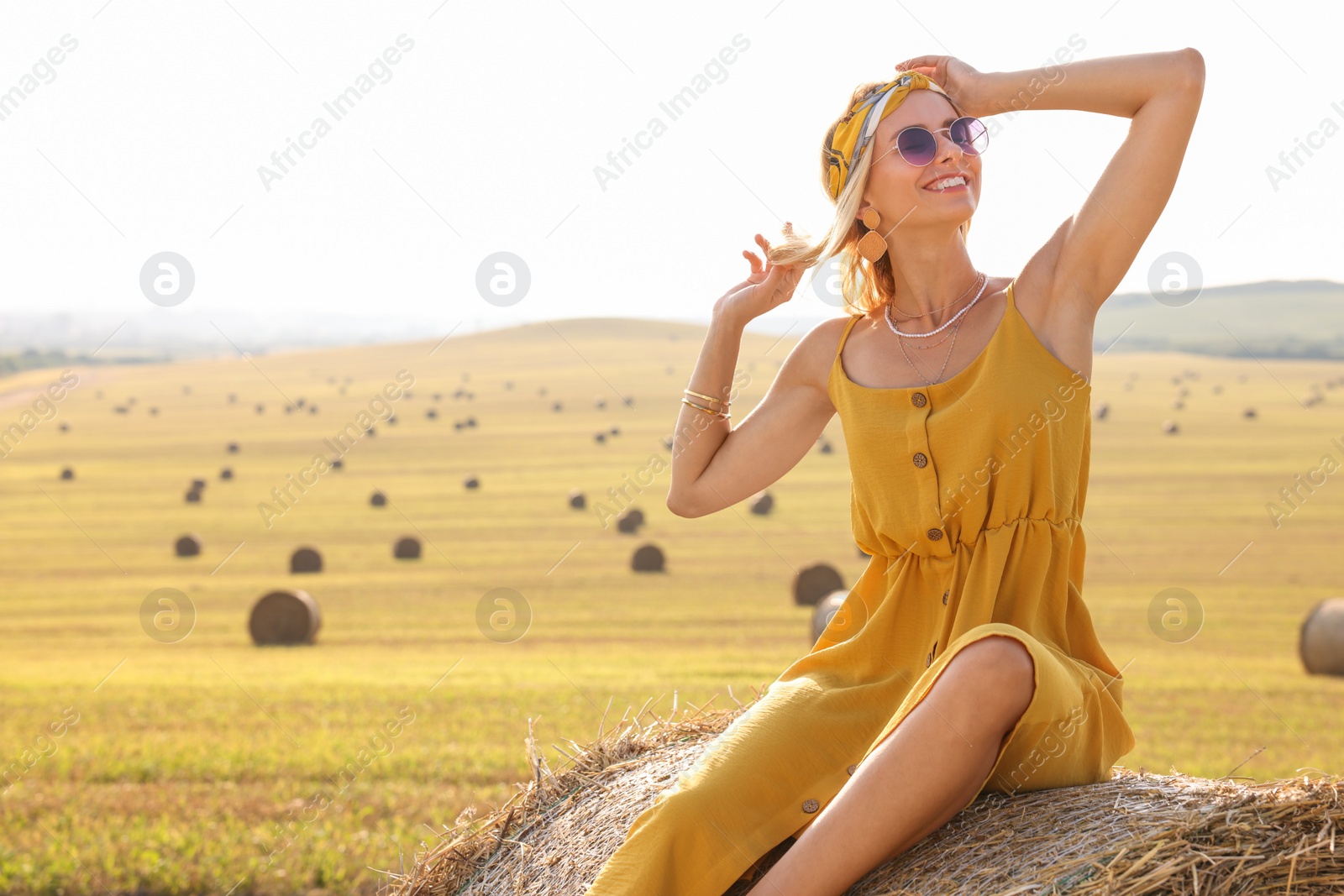 Photo of Beautiful hippie woman on hay bale in field, space for text