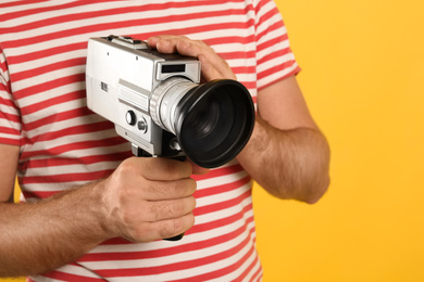 Man with vintage video camera on yellow background, closeup