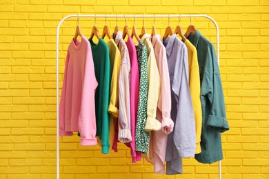 Photo of Rack with stylish clothes near yellow brick wall