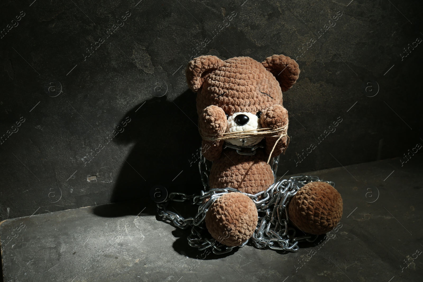 Photo of Stop child abuse. Chained toy bear covering eyes on dark grey background