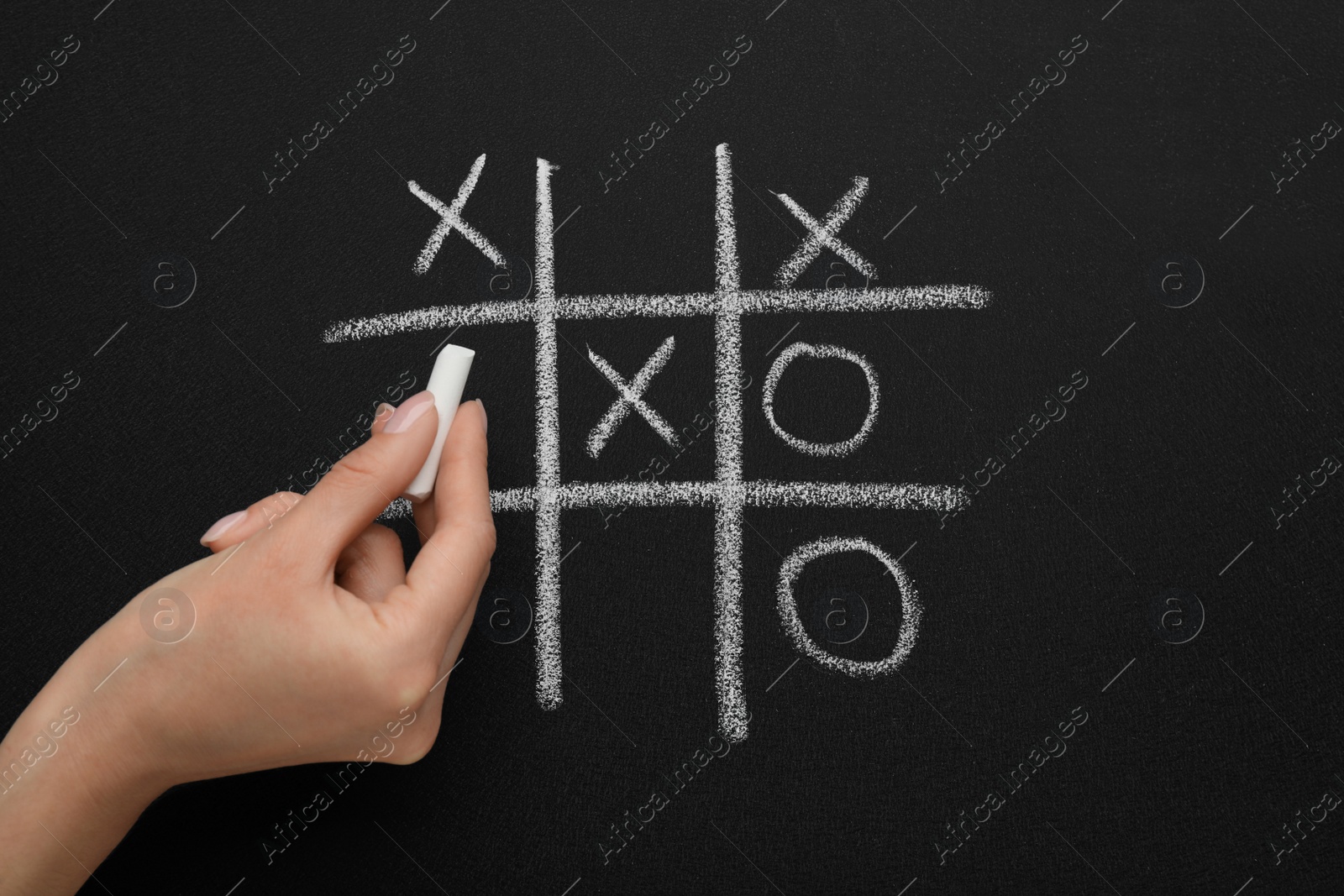 Photo of Woman playing tic tac toe game on blackboard, top view