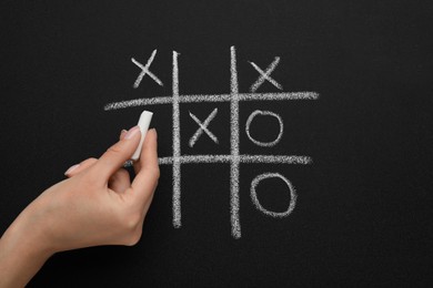 Photo of Woman playing tic tac toe game on blackboard, top view