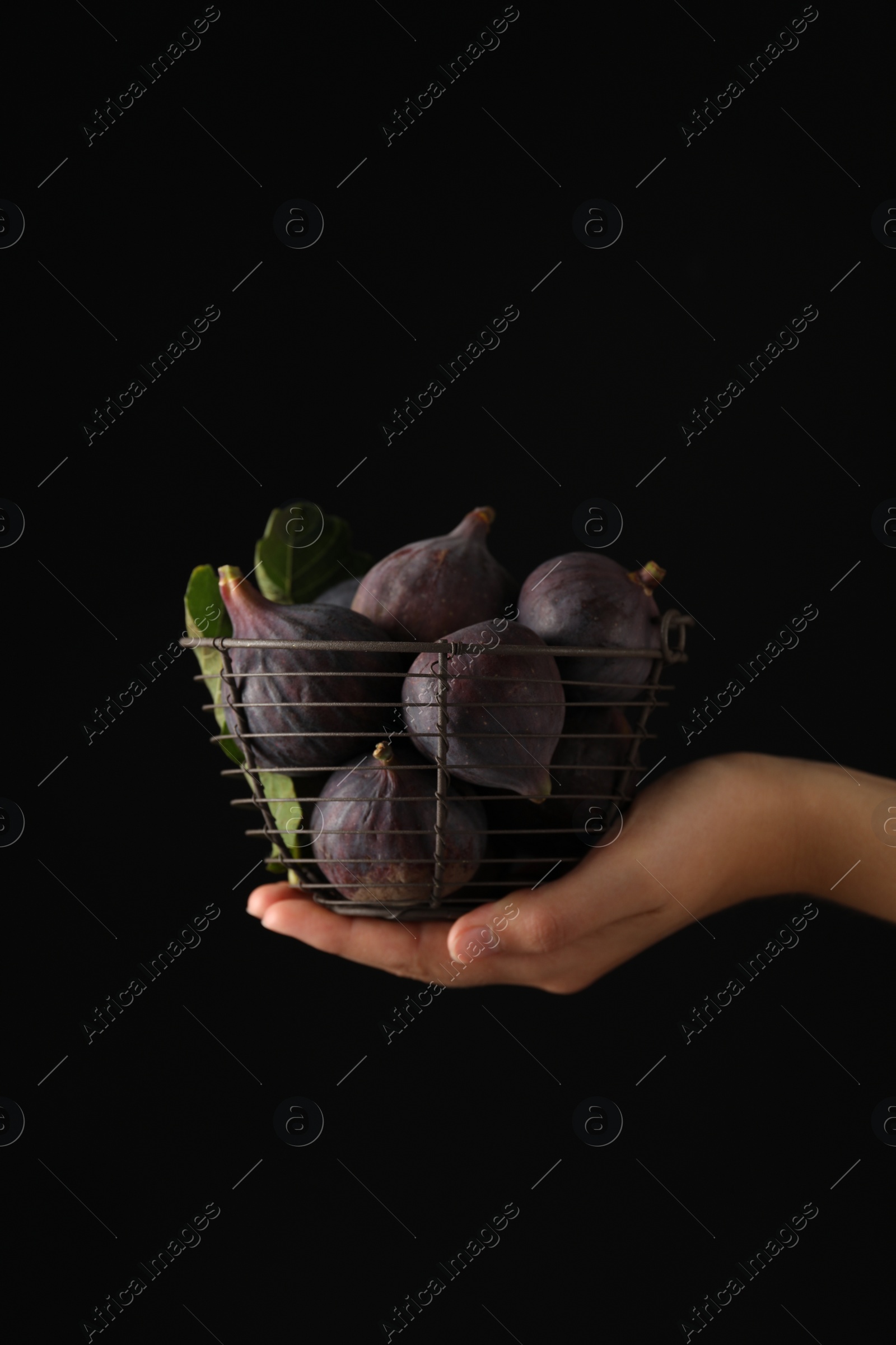 Photo of Woman holding basket with tasty raw figs on black background, closeup