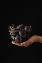Woman holding basket with tasty raw figs on black background, closeup