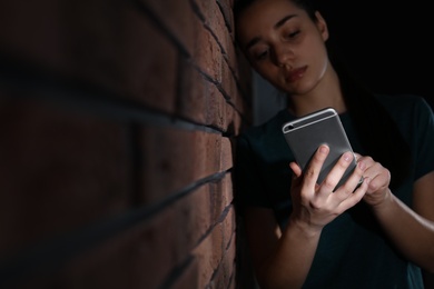 Photo of Sad woman with mobile phone near brick wall, space for text. Loneliness concept