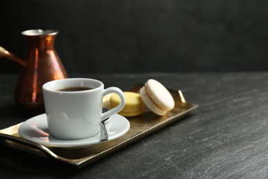 Tray with hot coffee in cup and macarons on dark textured table. Space for text