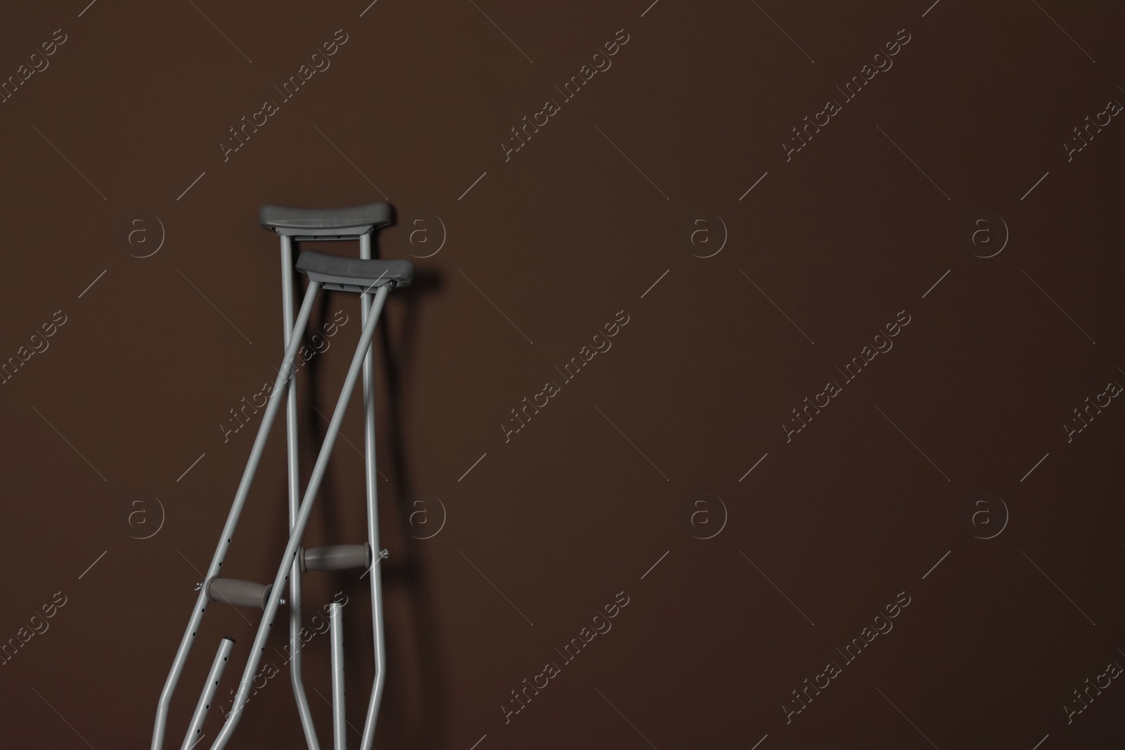 Photo of Pair of axillary crutches on brown background. Space for text