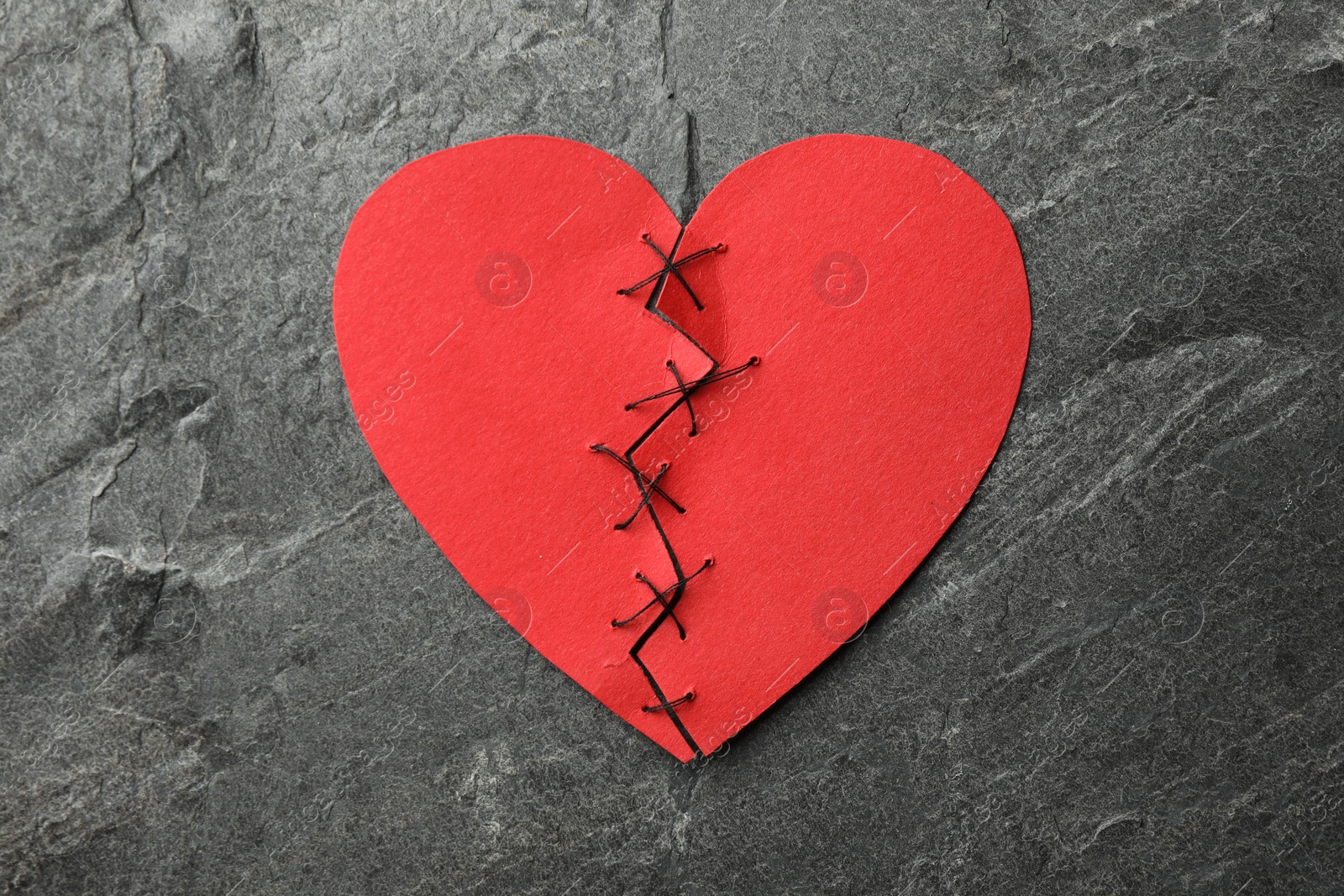 Photo of Broken heart. Torn red paper heart sewed with thread on dark grey table, top view