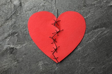 Photo of Broken heart. Torn red paper heart sewed with thread on dark grey table, top view