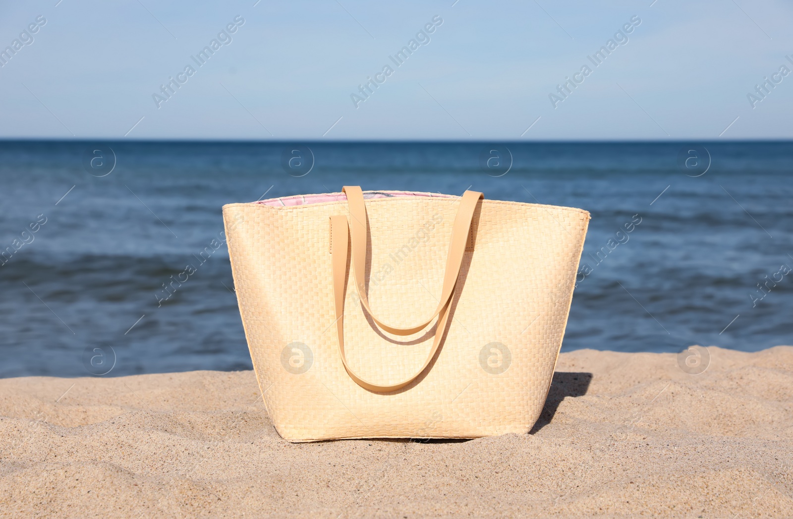 Photo of Stylish summer bag on sand near sea. Beach accessory