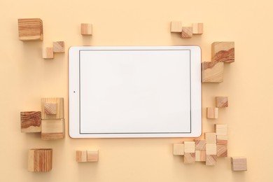 Modern tablet and wooden cubes on beige background, flat lay. Space for text