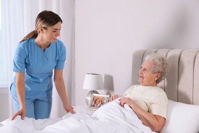 Photo of Young caregiver assisting senior woman in bedroom. Home health care service