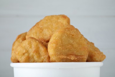 Photo of Bucket with tasty chicken nuggets on white wooden background, closeup