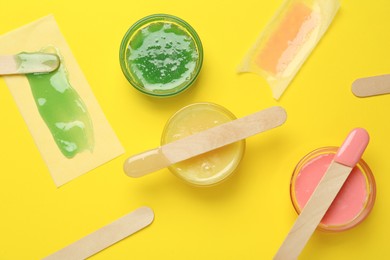 Photo of Flat lay composition with different types of wax and spatulas on yellow background