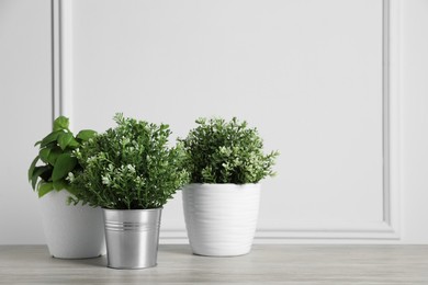 Photo of Different artificial potted herbs on wooden table near white wall, space for text