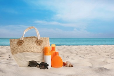 Bag with sunglasses and cosmetics on sunny ocean beach, space for text. Summer vacation