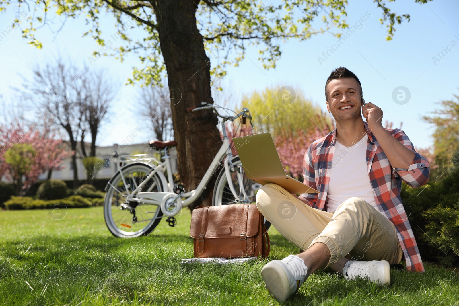 Photo of Man with laptop talking on phone in park