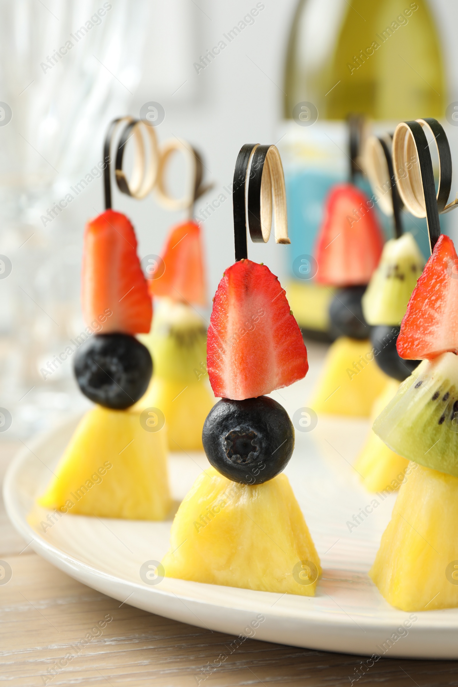 Photo of Tasty canapes with pineapple, kiwi and berries on light wooden table, closeup