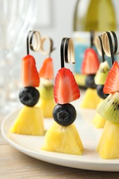 Photo of Tasty canapes with pineapple, kiwi and berries on light wooden table, closeup