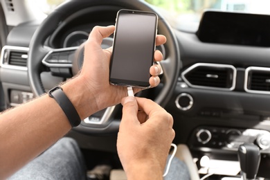 Man connecting charging cable to smartphone in car, closeup