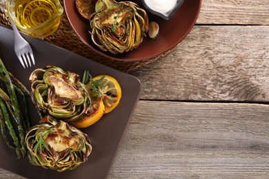 Photo of Tasty grilled artichokes served on wooden table, flat lay. Space for text