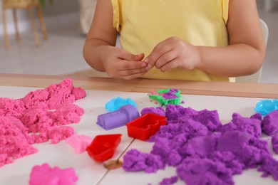 Photo of Little girl playing with bright kinetic sand at table indoors, closeup