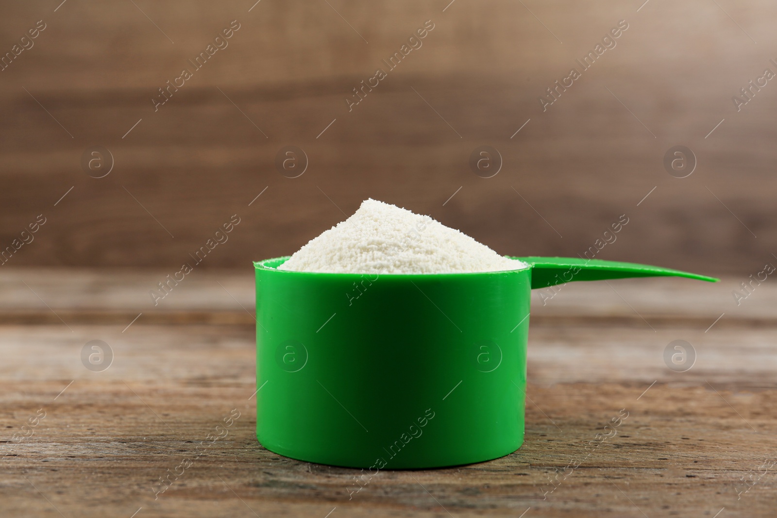 Photo of Measuring scoop of protein powder on wooden table, closeup