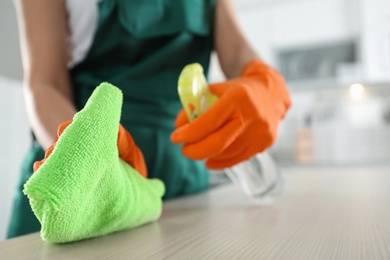 Photo of Worker in gloves cleaning table with rag, closeup. Space for text