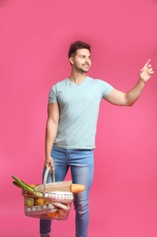 Young man with shopping basket full of products on pink background