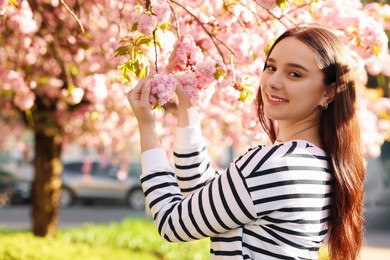 Beautiful woman near blossoming tree on spring day, space for text