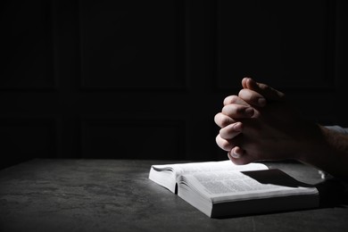 Photo of Religion. Christian man praying over Bible at table against black background, closeup. Space for text