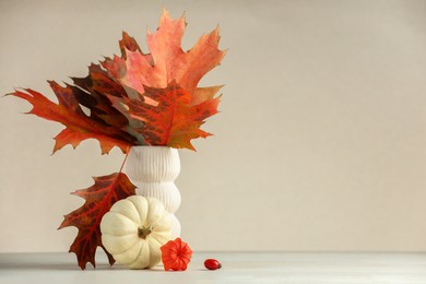 Photo of Beautiful autumn leaves in vase, pumpkin and physalis on table against beige background, space for text