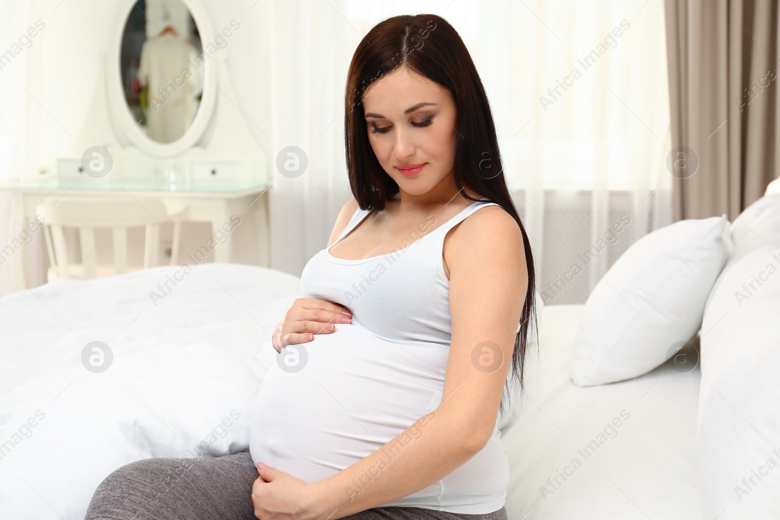 Photo of Beautiful pregnant woman sitting on bed at home