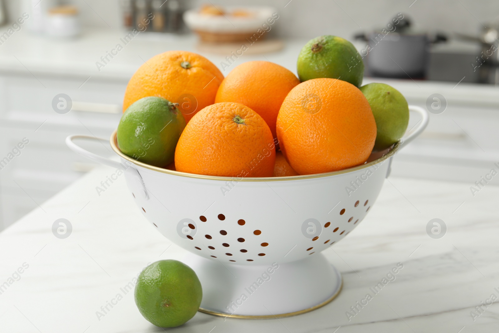 Photo of Colander with fresh fruits on white marble table in kitchen