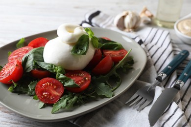 Delicious burrata cheese served with tomatoes and basil on white wooden table, closeup