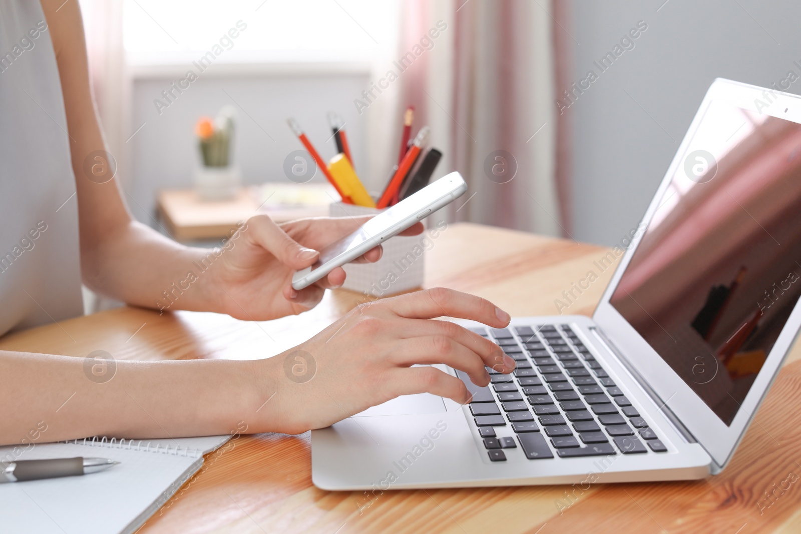 Photo of Young woman working with mobile phone and laptop at desk. Home office