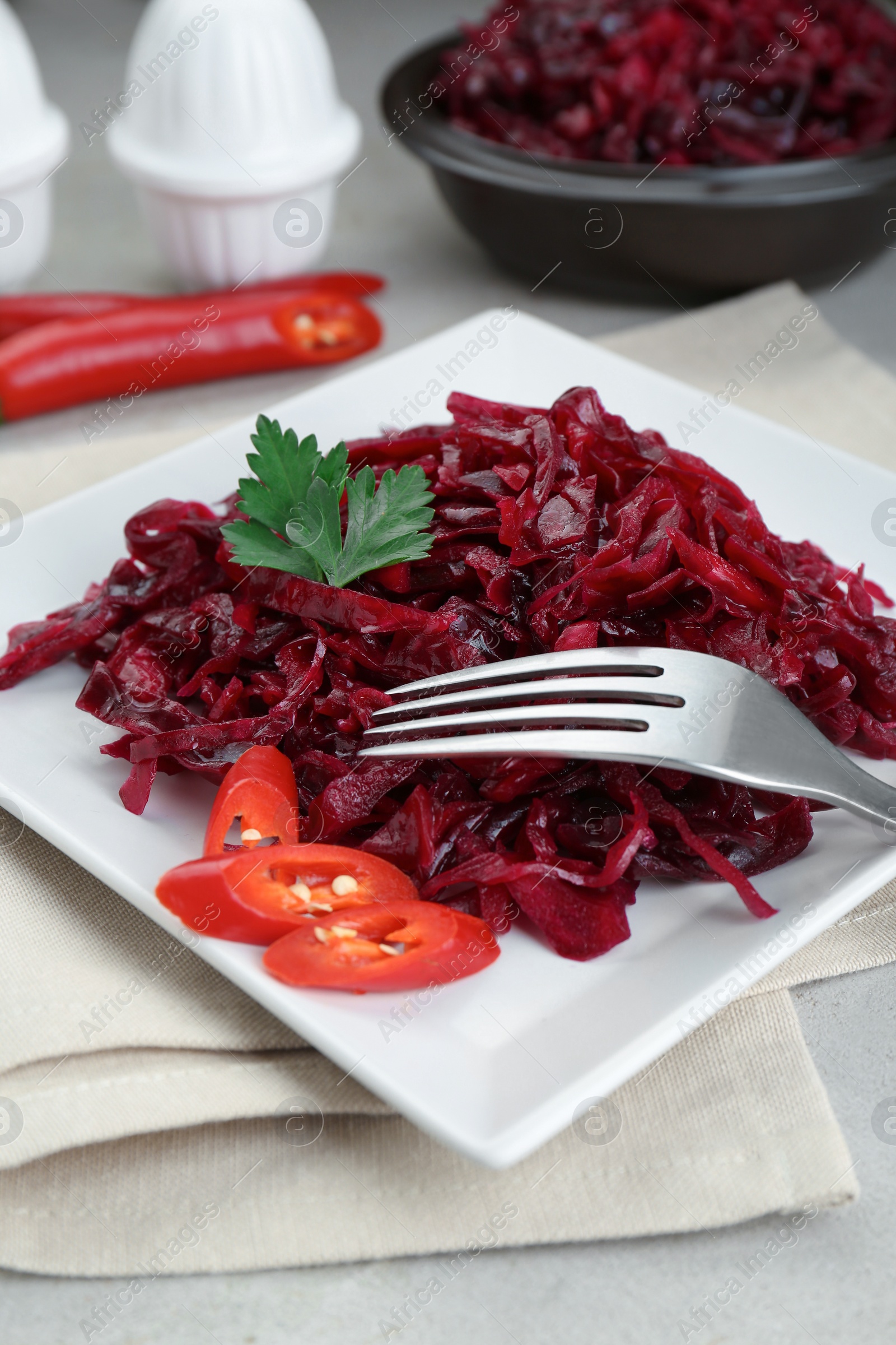 Photo of Tasty red cabbage sauerkraut with chili pepper and parsley served on light table