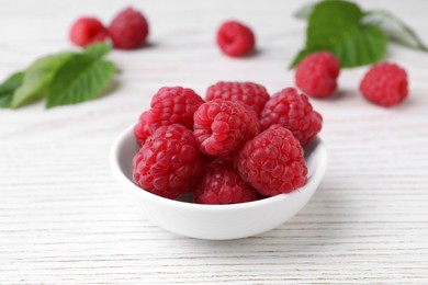 Photo of Tasty ripe raspberries in bowl on white wooden table