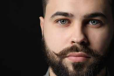 Handsome young man with mustache on black background, closeup