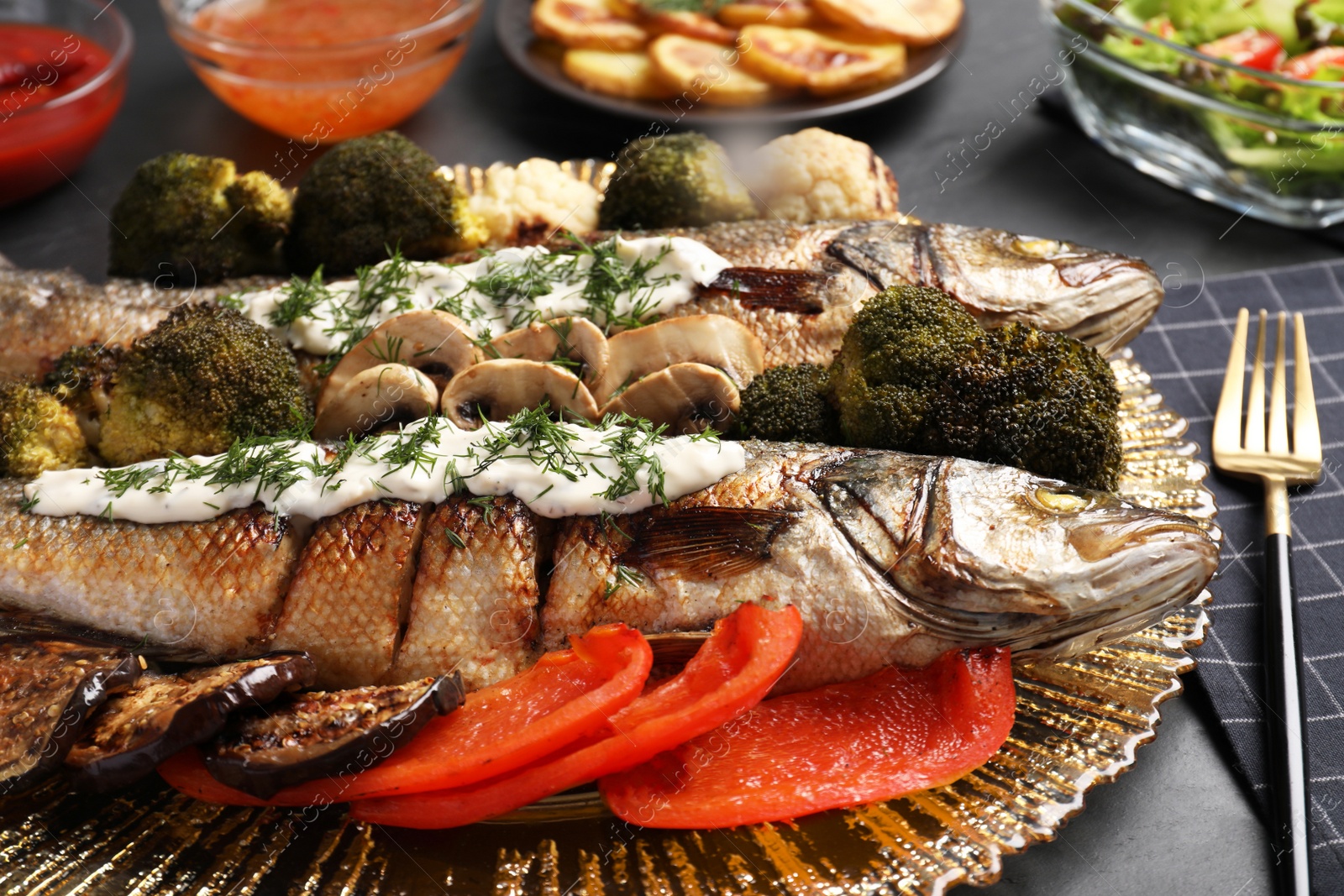 Photo of Delicious baked sea bass fish with sauce on dark table, closeup