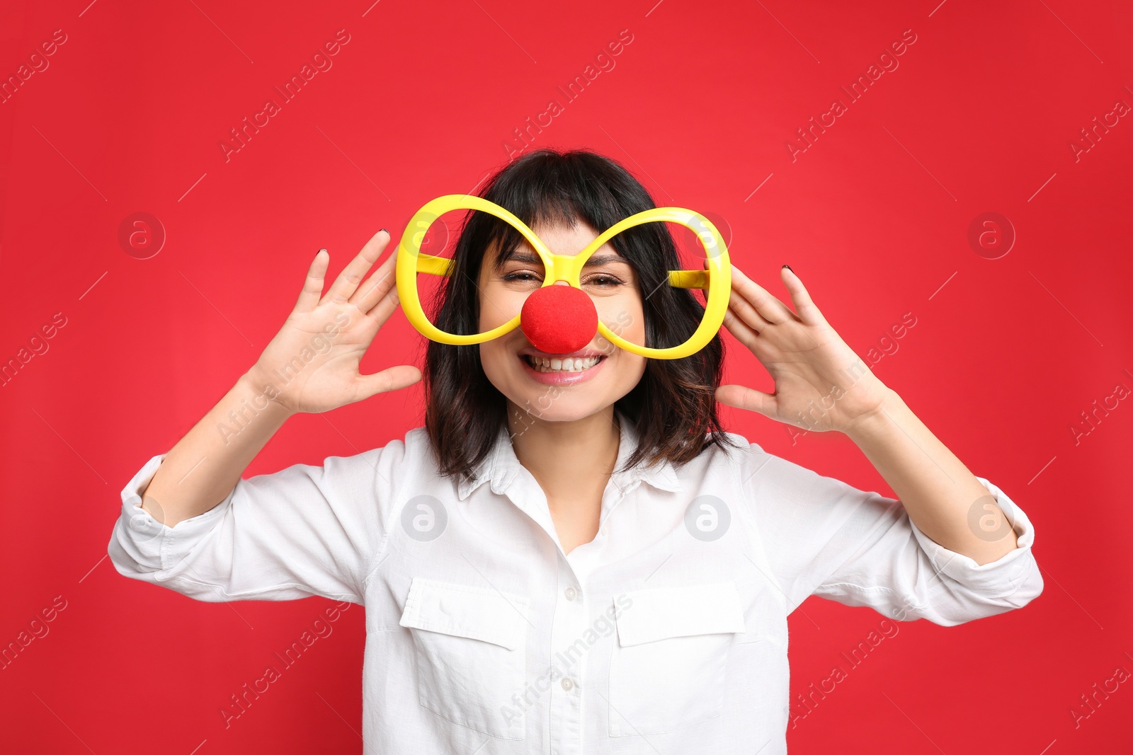 Photo of Joyful woman with large glasses and clown nose on red background. April fool's day