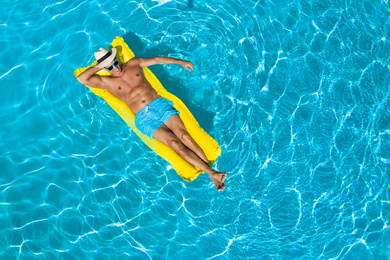 Image of Young man with inflatable mattress in swimming pool, top view. Space for text