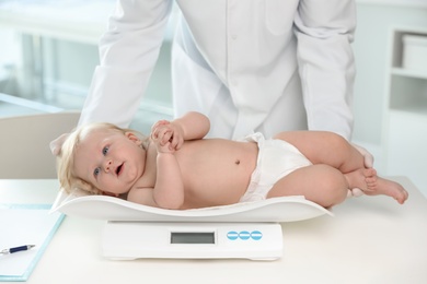 Photo of Pediatrician weighting baby on scale in hospital. Healthy growth