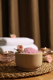 Bowl of pink sea salt, roses, burning candles and towels on wooden table