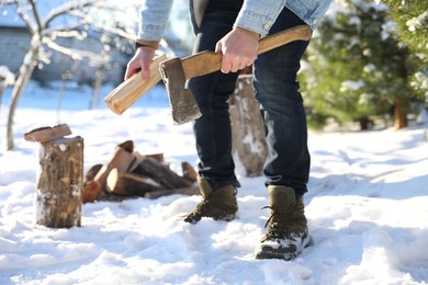 Photo of Man chopping wood with axe outdoors on winter day, closeup