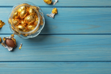 Photo of Chocolate eggs wrapped in golden foil on light blue wooden table, flat lay. Space for text