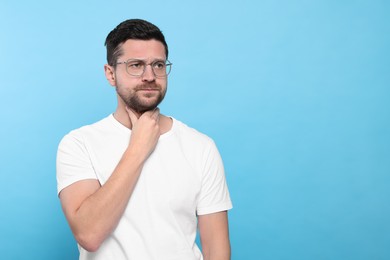 Photo of Man suffering from sore throat on light blue background, space for text